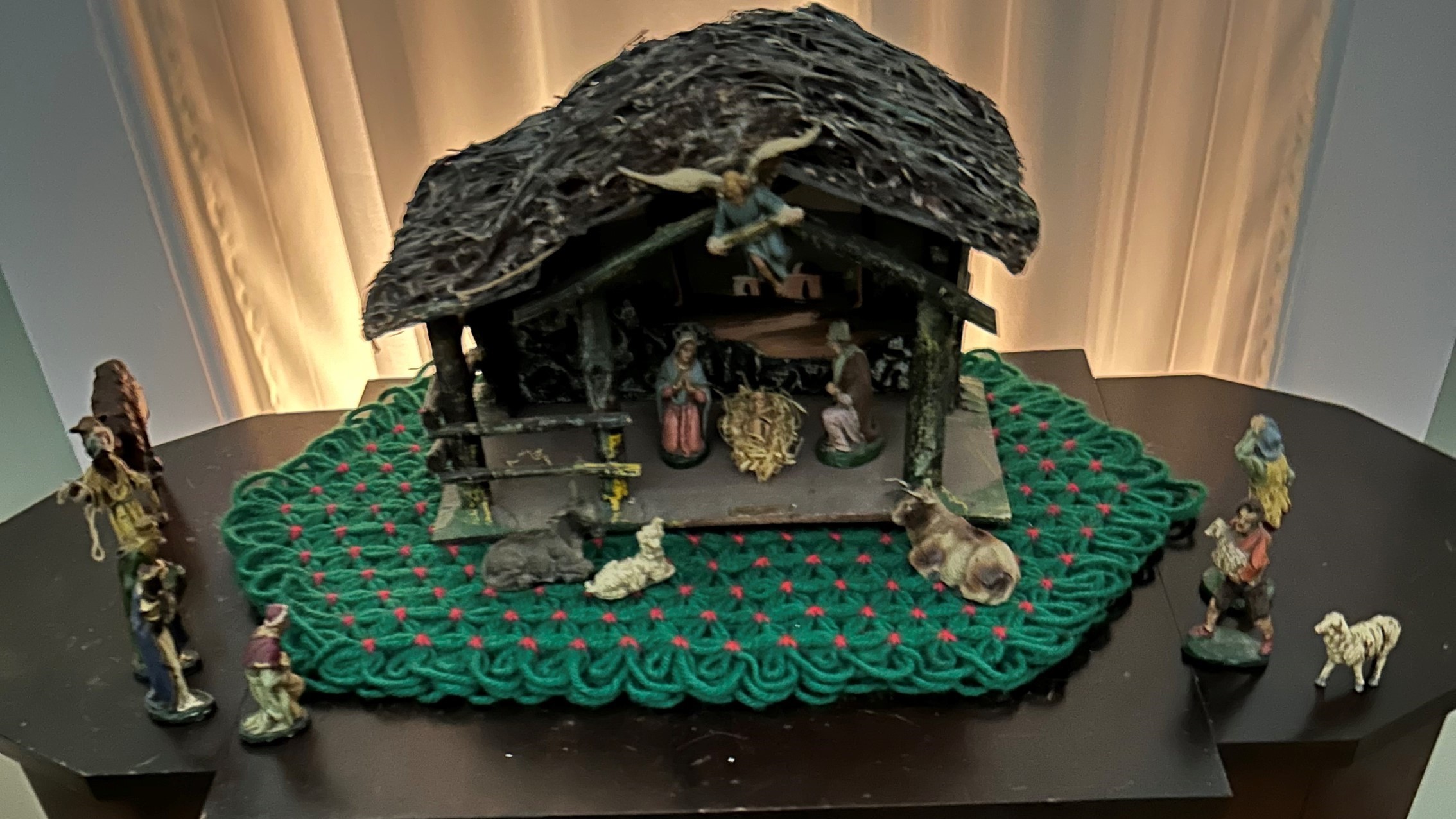 A nativity scene displayed on a green mat with red accents features a stable with figures of Mary, Joseph, baby Jesus, angels, wise men, and various animals.