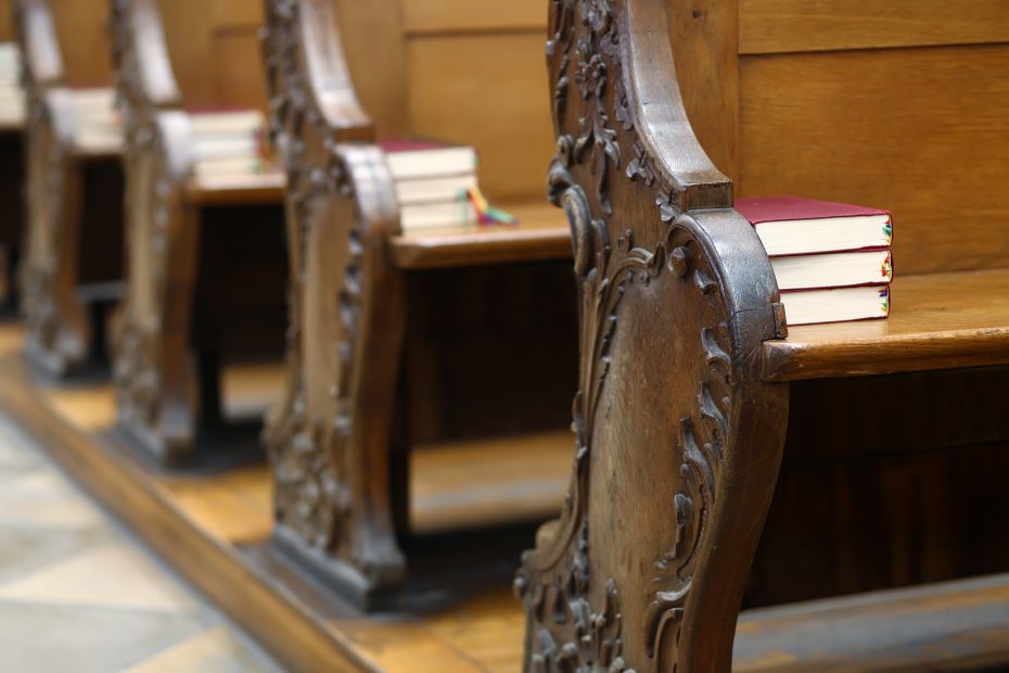 Wooden pews with intricate carvings, holding stacked hymnbooks, in an empty church.