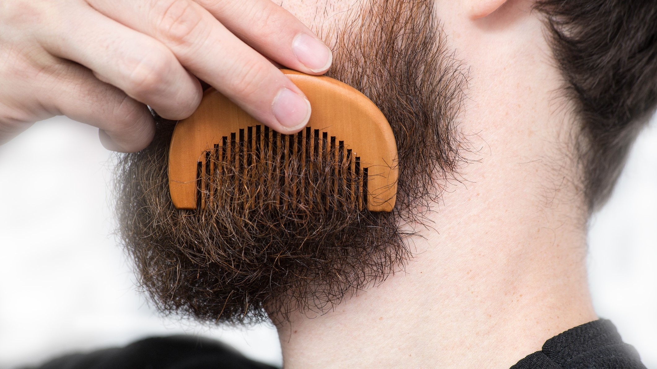 A close-up of a person combing their beard with a wooden comb.