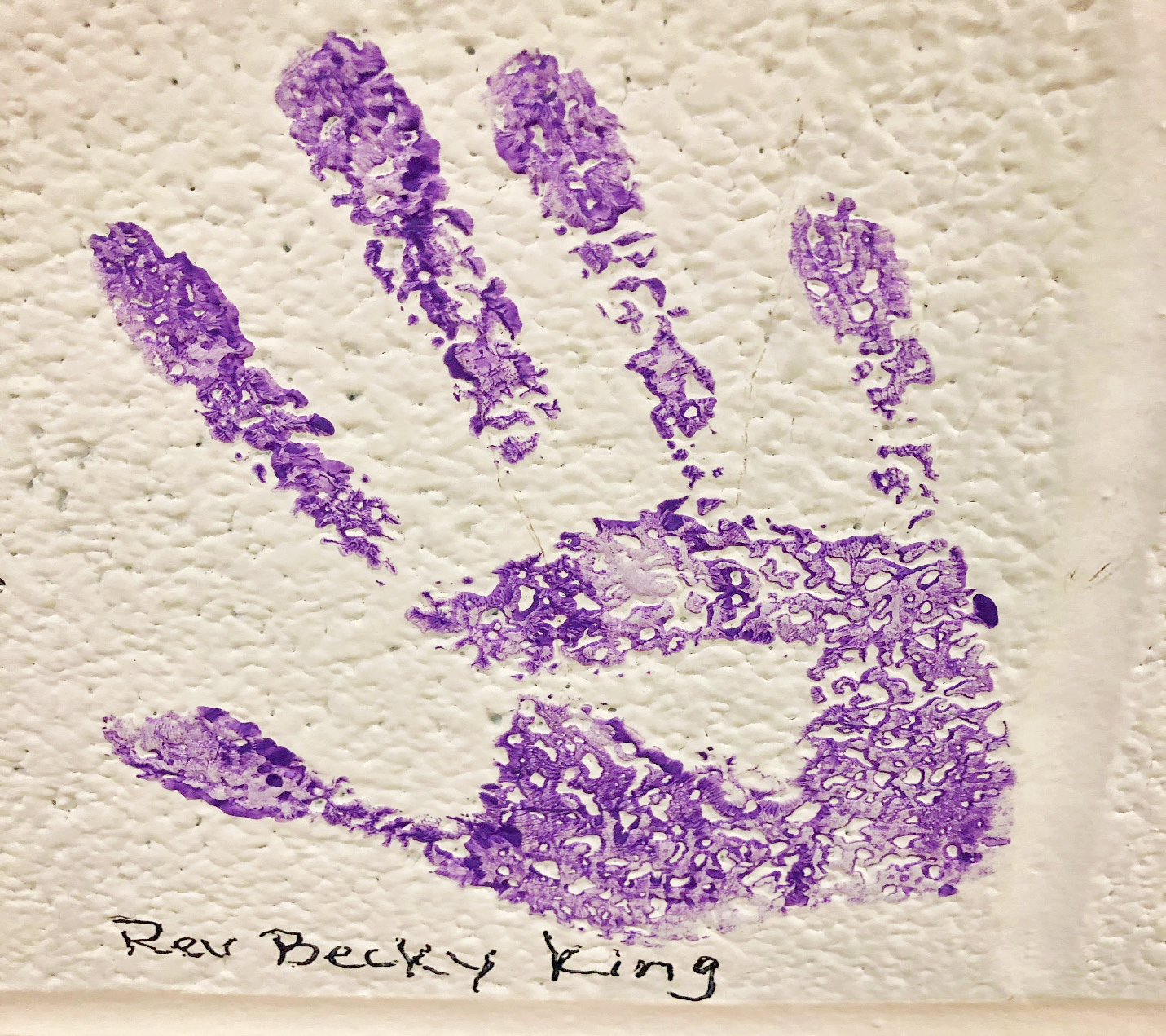 A purple handprint labeled "Rev. Becky King" on a textured white wall.