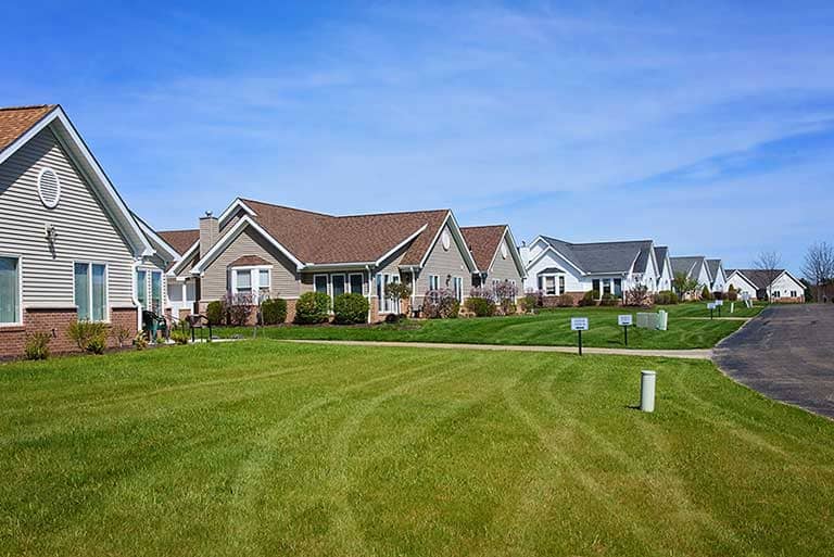 A row of single-story suburban houses with well-maintained lawns under a clear blue sky.