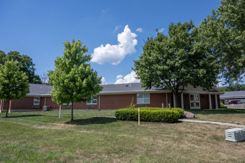 A single-story red-brick building with multiple trees and a well-manicured lawn under a clear blue sky.