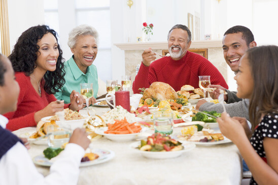 A family of six, seated around a table, enjoys a festive meal together, with a turkey as the centerpiece and various side dishes. They are smiling and appear engaged in conversation.