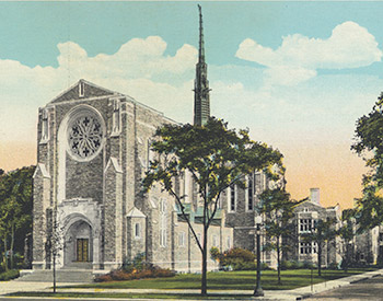 A stone church with a tall spire, surrounded by trees and green lawns, under a partly cloudy sky. The building has large arched windows and a prominent circular window on its facade.