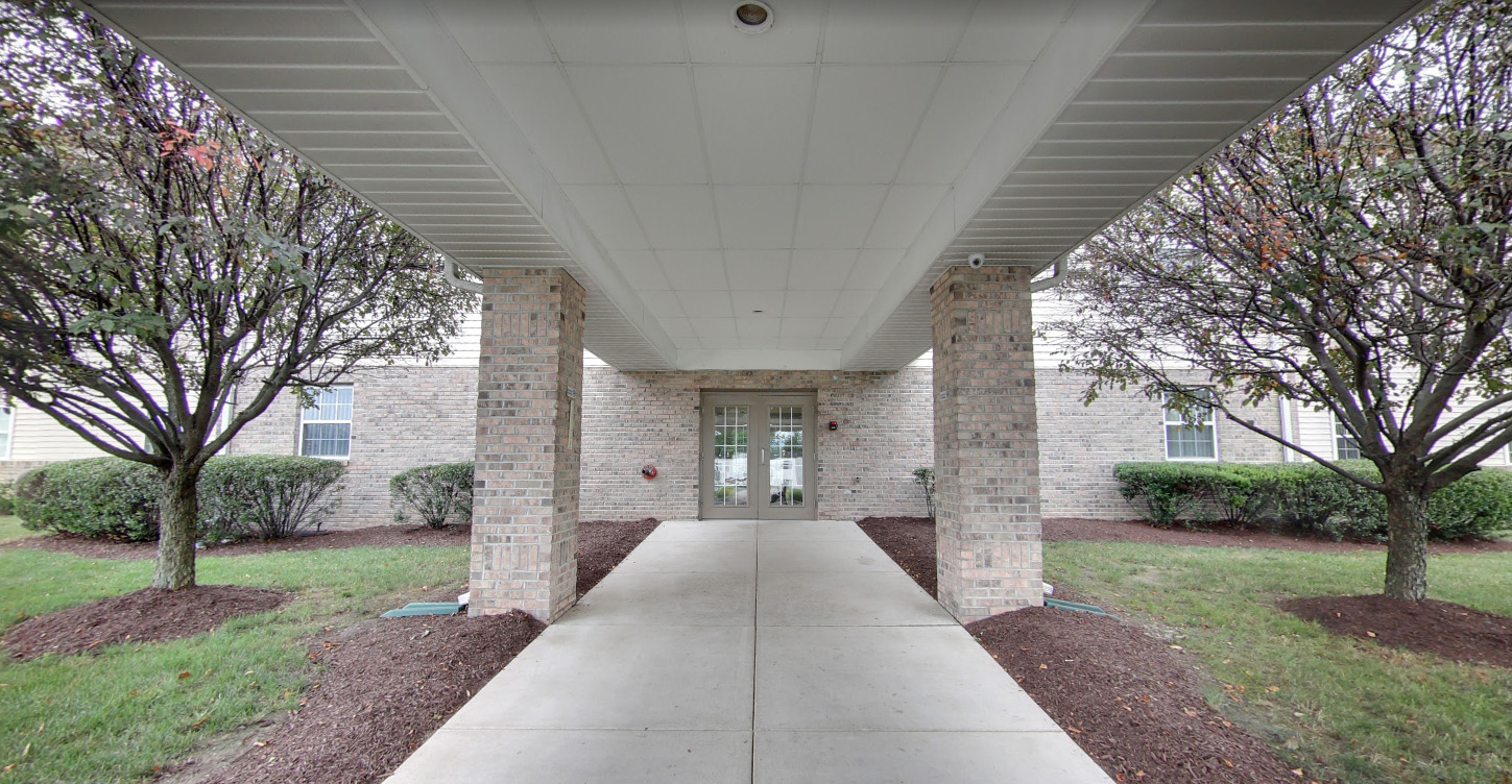 Covered entryway with brick columns leading to a glass door entrance, flanked by trees and shrubs on both sides. United Church Homes Expands to 15 States, enhancing community atmospheres just like this inviting entrance.