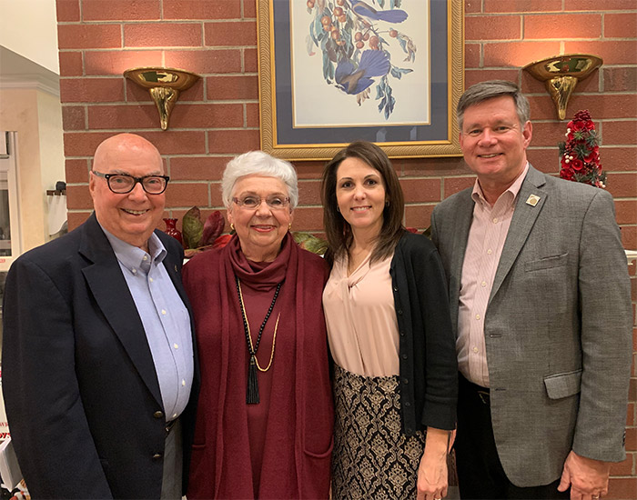 Four adults posing together in a warmly lit room with brick walls and framed artwork in the background.