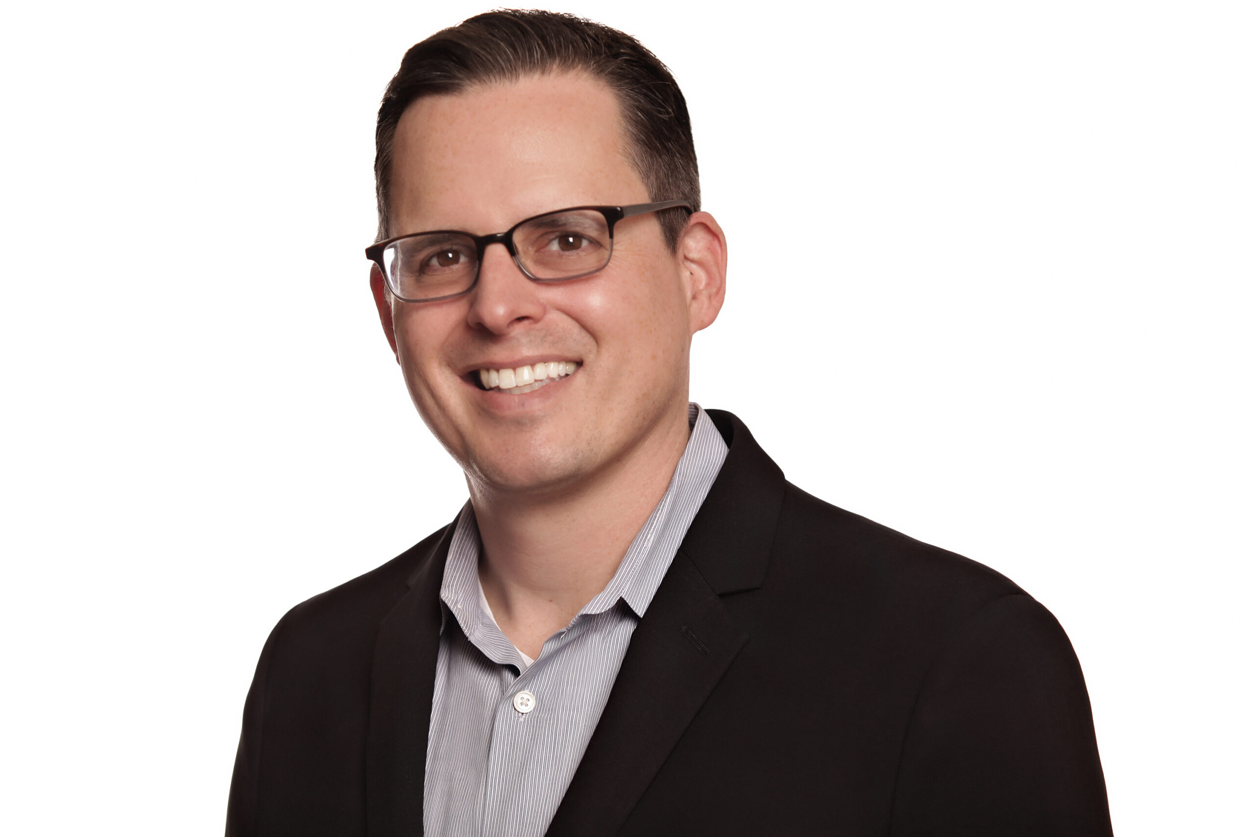 A man with short dark hair and glasses, wearing a black blazer over a light gray collared shirt, smiles at the camera against a white background, as United Church Homes prepares to welcome its Senior Executive Vice President.