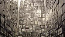 Tall walls covered with numerous framed black-and-white photographs in a narrow room, creating a dense, historical visual collage.