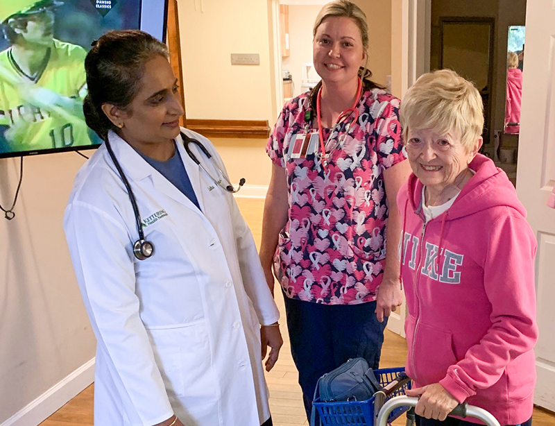 A medical director, a doctor, and a nurse stand with an elderly woman who uses a walker in a healthcare facility.