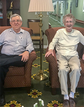 An elderly man and woman are sitting in armchairs in a well-lit room.