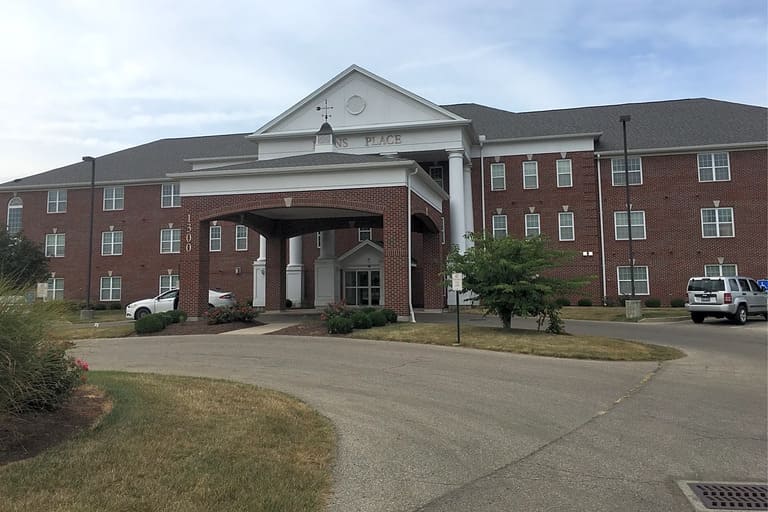 A three-story brick building with a covered entrance and a circular driveway stands proudly as an icon of affordable housing in Dayton, Ohio. The sign above the entrance reads "PLACE." Multiple windows are visible on each floor.