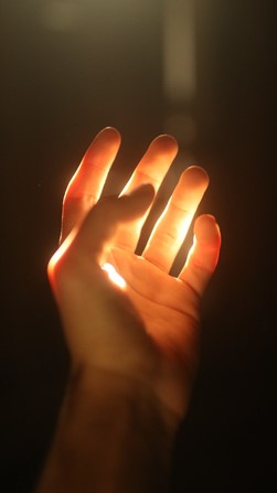 A hand is held up with fingers spread apart against a bright light source, creating a dramatic contrast between the illuminated hand and the dark background.