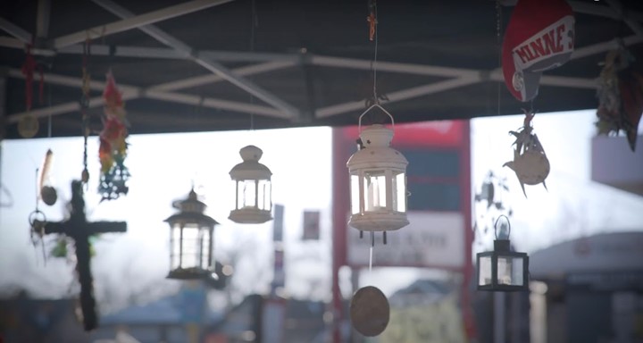 A market stall display showing various hanging decorative items, including lanterns, a cross, and other ornaments, with a blurred backdrop of a double-decker bus.