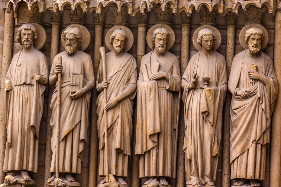 Five stone statues of saints or apostles, each holding different objects, are intricately carved into the façade of a historic building.