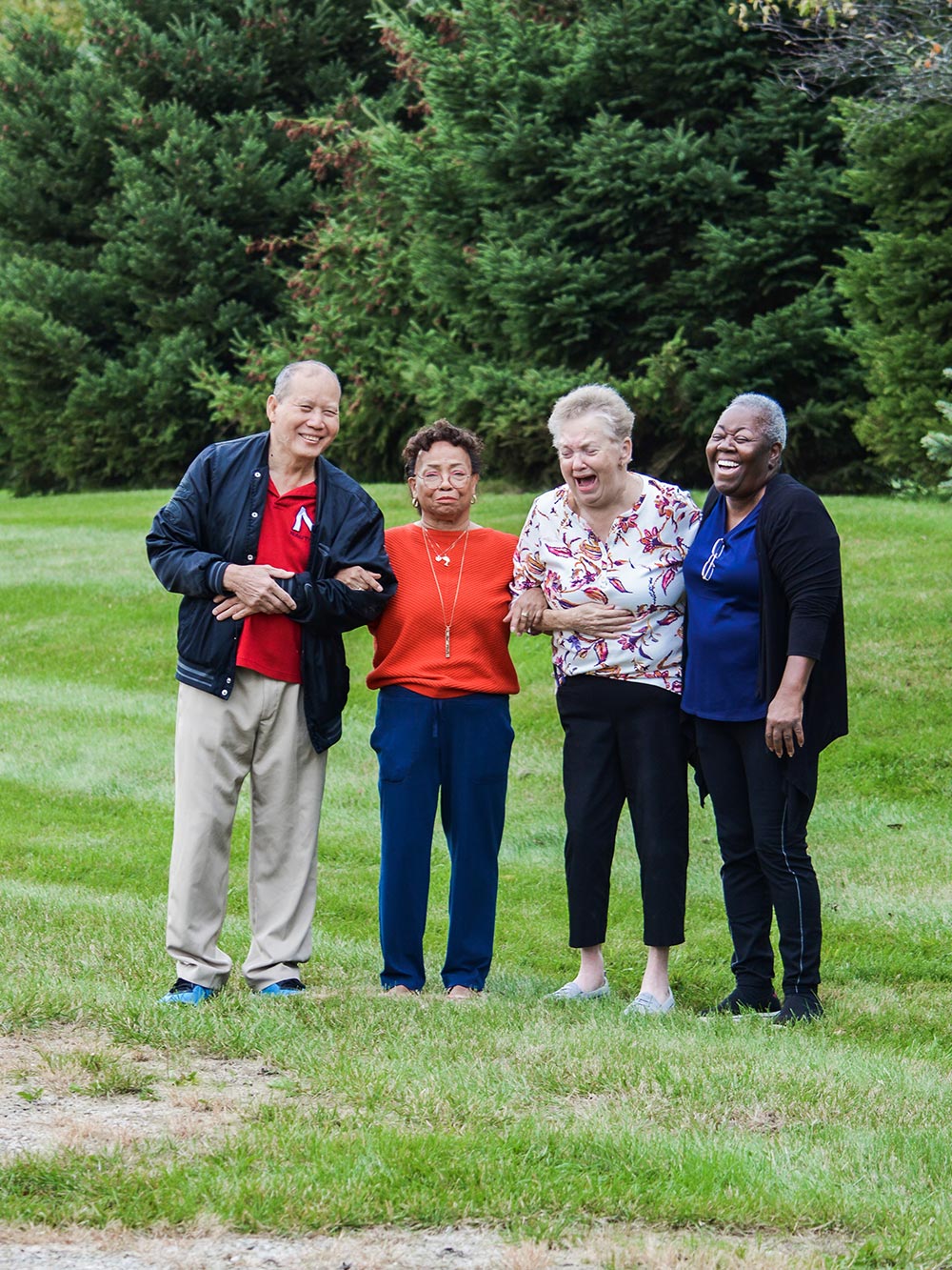 Four elderly individuals are standing together outdoors, smiling and holding each other’s arms. Trees and grass are visible in the background, illustrating a sense of community and joy that aligns with the values promoted by careers at United Church Homes.