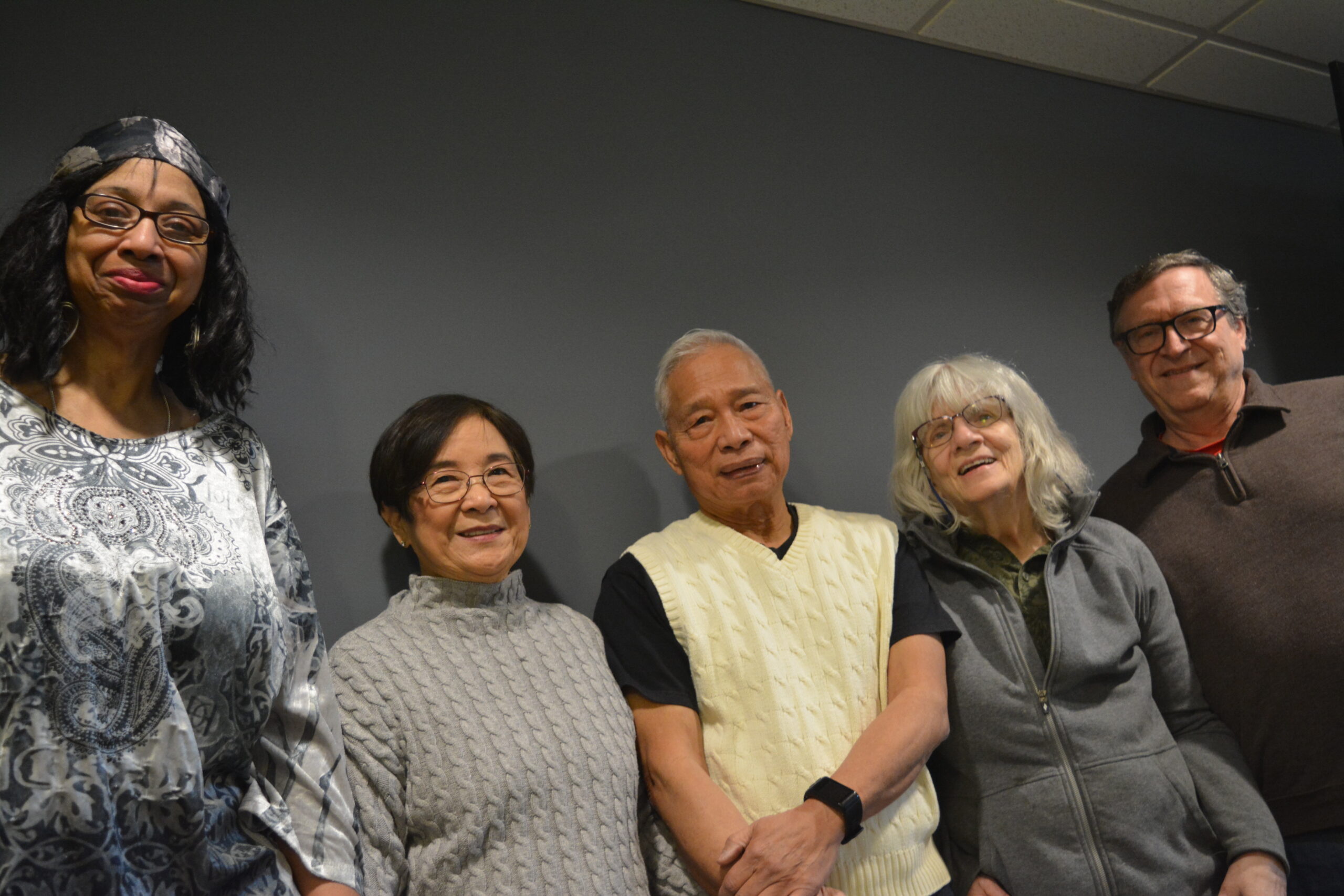 Five people stand side by side against a plain wall, smiling at the camera. They are dressed in casual clothing and their expressions radiate what is abundant life: joy existing in large amounts, marked by great plenty.