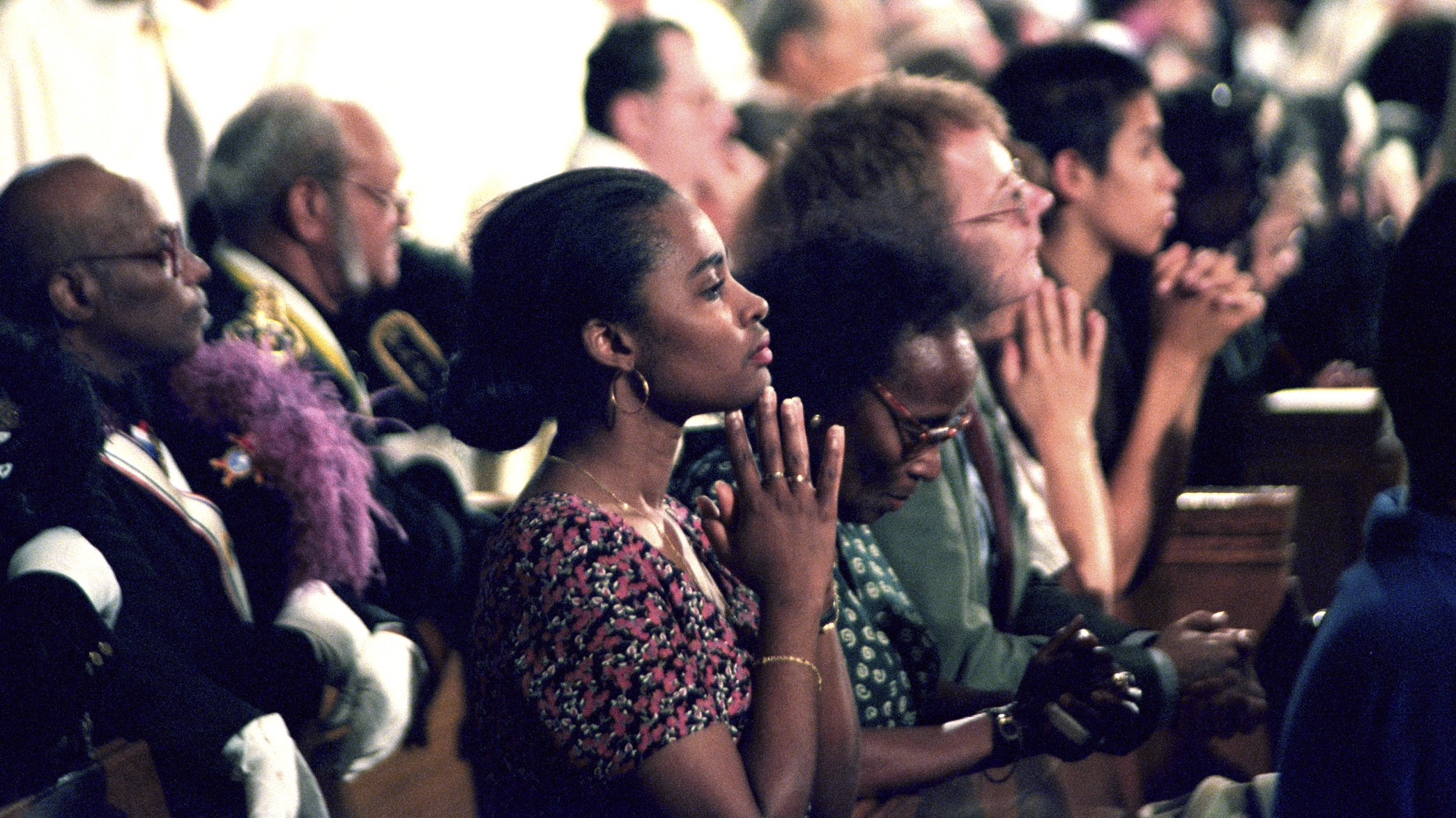 A diverse group of people sitting in prayer with hands clasped in a church.