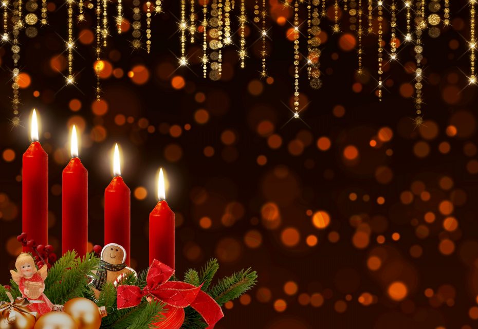 Four lit red candles with Christmas ornaments and greenery are in the foreground. Bright golden bokeh and hanging decorations create a festive background.