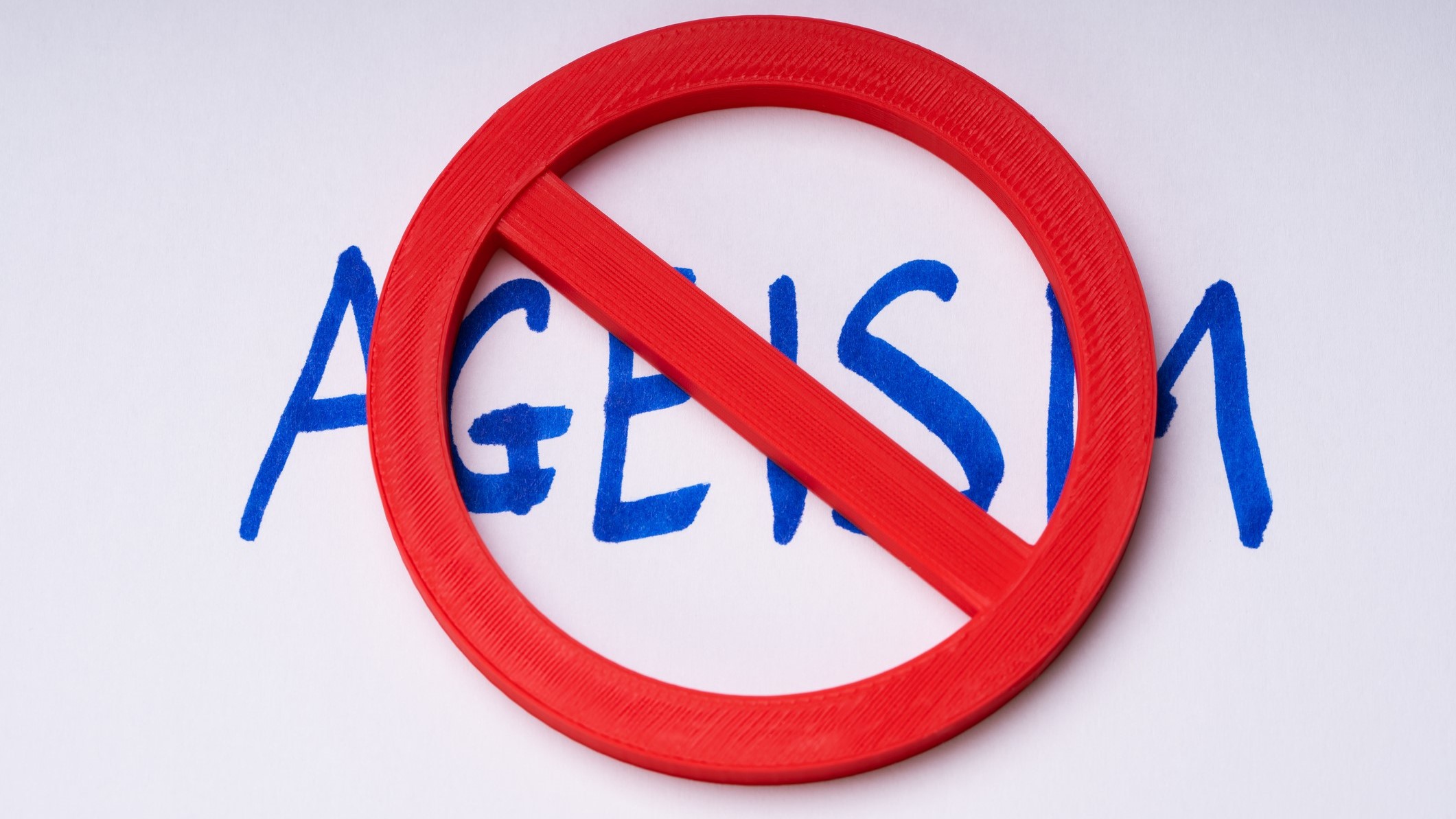 A red prohibition symbol is placed over the word "AGEISM," indicating opposition to age-based discrimination.