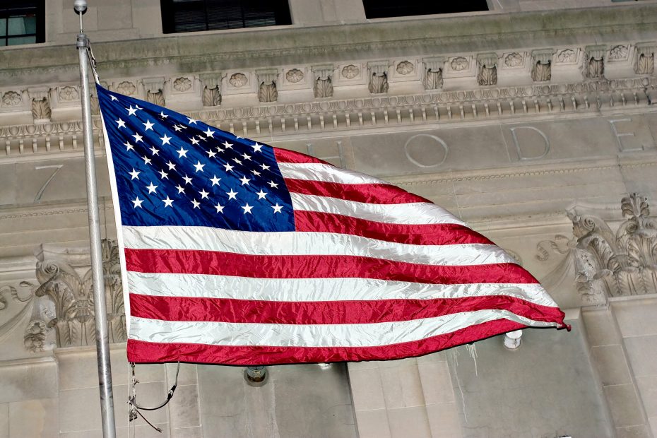 An American flag waves in front of a stone building.