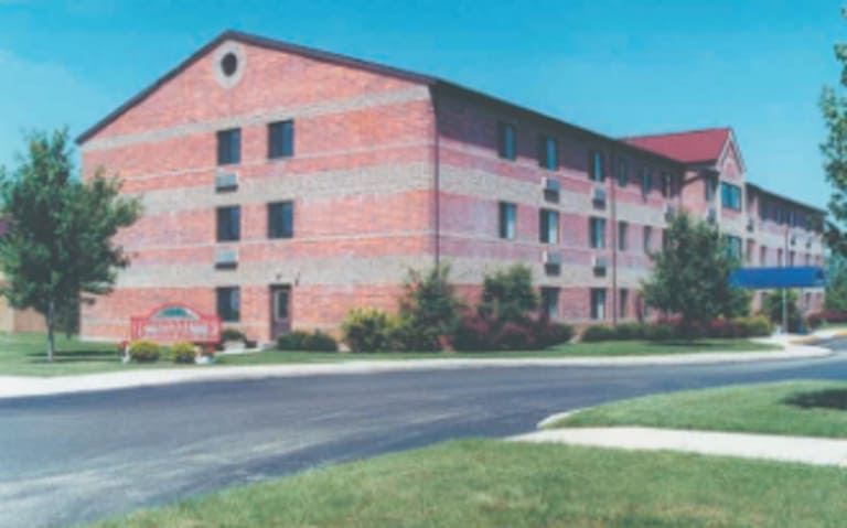 A three-story, red-brick building with a pitched roof, surrounded by trees and manicured lawns, represents affordable housing in Marion, Ohio. The entrance features a red canopy and an adjacent sign.