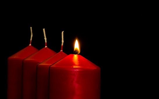 Four red candles arranged in a row against a black background, with only the second candle lit.