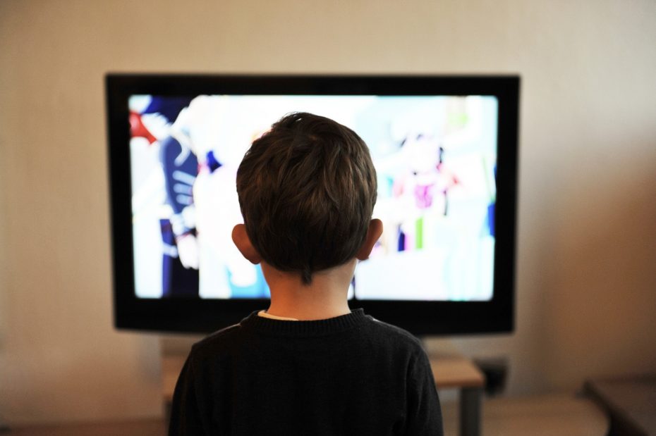 A child with short brown hair is watching a cartoon on a flat-screen television.