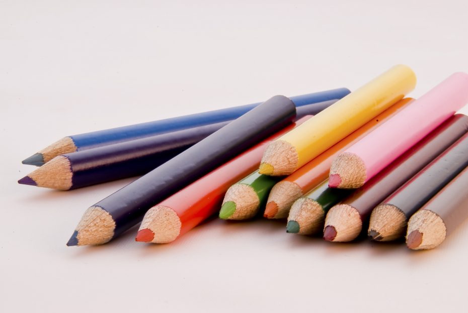 A group of colored pencils arranged on a white surface, displaying a variety of colors including blue, yellow, pink, green, and brown.