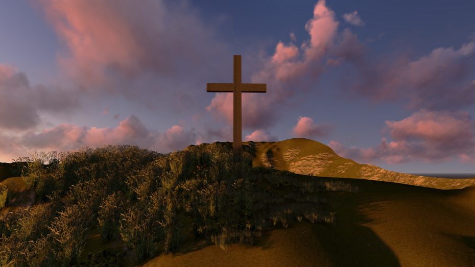 A large wooden cross stands on a grassy hill under a sunset sky with scattered clouds.