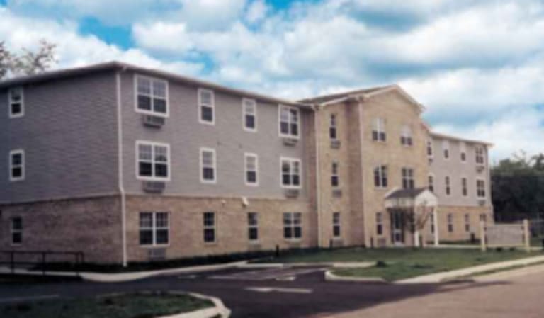 A three-story building with a combination of brick and siding exterior, featuring multiple windows and a small entrance canopy, set against a partly cloudy sky, exemplifies the charm of affordable housing in Lincoln Heights, Ohio.