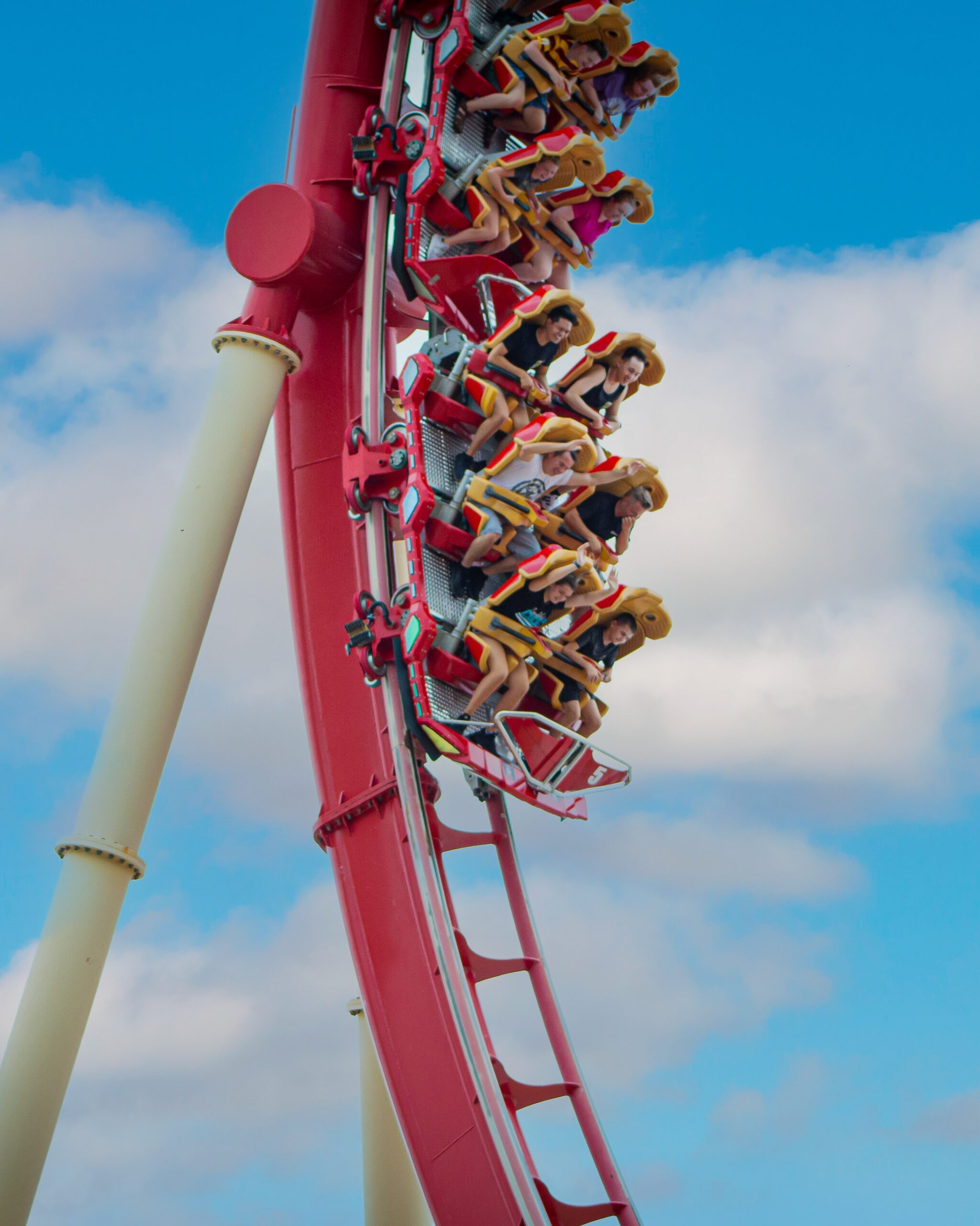 People riding a looping red roller coaster against a blue sky with clouds.