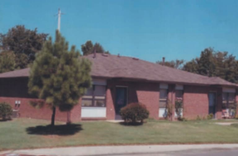 A single-story brick building with a gabled roof serves as affordable housing in Memphis, Tennessee. It is surrounded by trees and a lawn, with a small tree in front of the building.