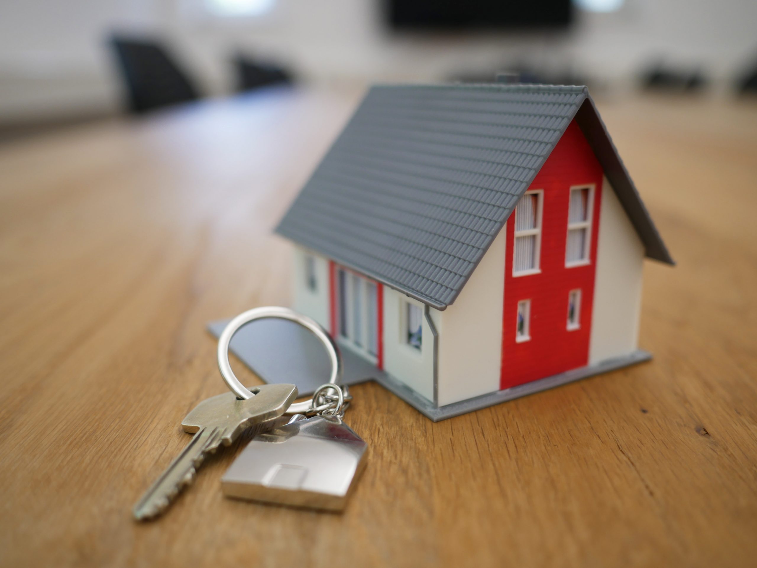 A miniature house model with a grey roof and red wall sits on a table next to a set of silver keys on a keyring. Is it time to sell?