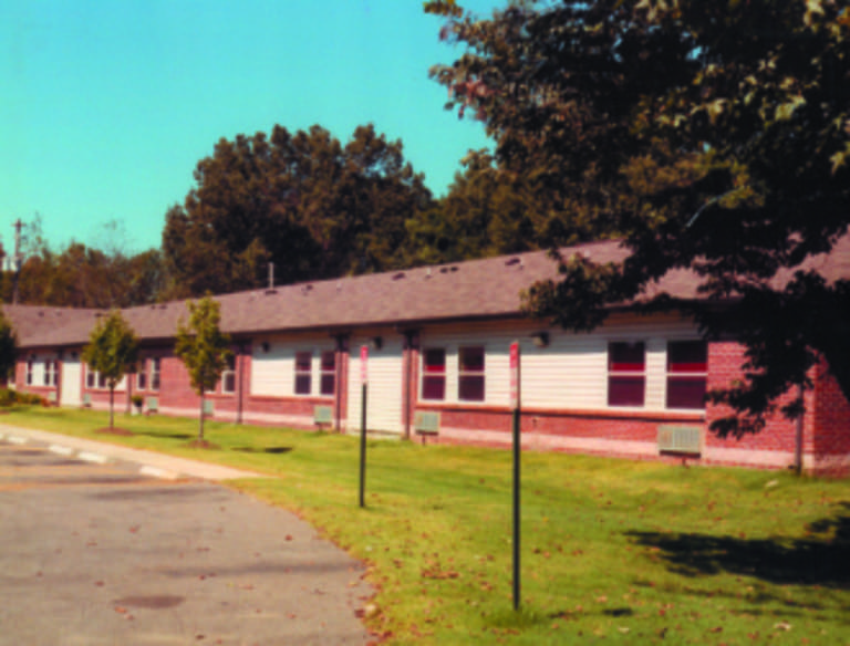 A single-story brick building with white siding and multiple windows, surrounded by trees and grass, seen on a clear day, exemplifies affordable housing in Memphis, Tennessee.